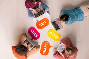 Four people in a circle using their computers with the words share, like , click, and hello in talk bubbles.